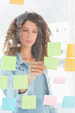 Focused pretty designer looking at sticky notes on window