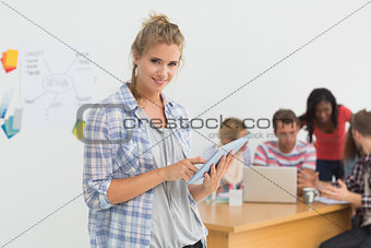 Smiling young designer using her tablet pc in front of her colleagues