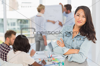 Asian woman smiling at camera while her colleagues are working