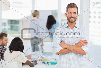 Handsome man smiling at camera while his colleagues are working