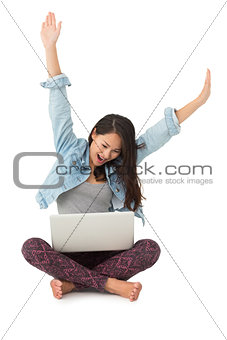 Asian woman cheering with laptop sitting on floor