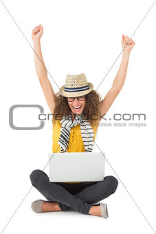 Pretty woman cheering at camera with laptop sitting on floor