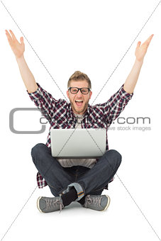 Handsome man cheering at camera with laptop sitting on floor