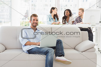 Young smiling designer working on his laptop on the couch