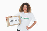 Happy volunteer holding a box of donations with hand on hip