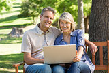 Happy couple using laptop in park