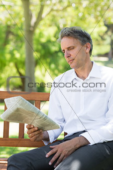 Businessman reading newspaper in park