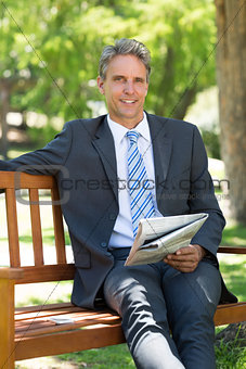 Businessman with newspaper sitting in park