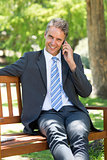 Businessman answering smart phone on park bench