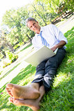 Businessman with laptop sitting on parkland