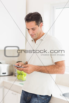 Side view of a man text messaging in kitchen