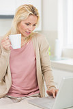 Beautiful woman with coffee cup using laptop in kitchen