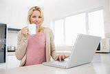 Portrait of beautiful woman with coffee cup using laptop in kitchen