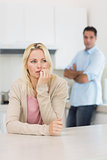 Thoughtful woman with blurred man in background in kitchen