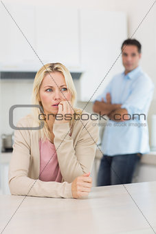 Thoughtful woman with blurred man in background in kitchen