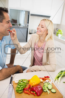 Happy loving woman feeding man vegetable in kitchen