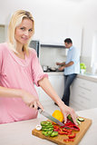 Woman chopping vegetables with man doing dishes at kitchen