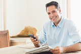 Smiling casual man with newspaper and cellphone in kitchen