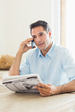 Casual man with newspaper using cellphone in kitchen