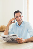 Casual man with newspaper using cellphone in kitchen