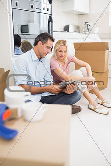 Couple using digital tablet amid boxes in house