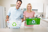 Smiling couple carrying recycling containers in kitchen