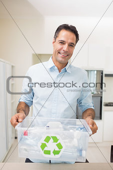 Smiling man carrying recycling container in kitchen