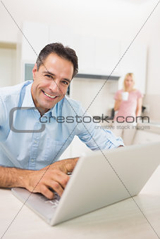 Man using laptop with woman drinking coffee at kitchen