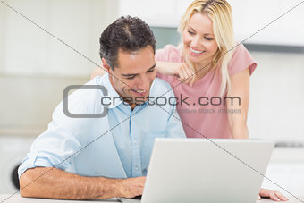 Happy couple using laptop in kitchen