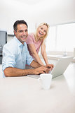 Portrait of cheerful couple using laptop in kitchen
