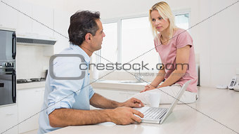 Serious couple with laptop sitting in kitchen