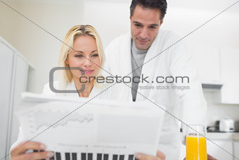 Couple in bathrobes reading newspaper in kitchen