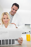 Smiling couple in bathrobes reading newspaper in kitchen