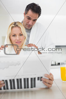 Couple in bathrobes reading newspaper in kitchen