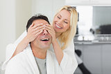 Smiling woman covering happy mans eyes in kitchen