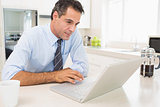 Concentrated well dressed man using laptop in kitchen
