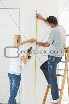 Rear view of a couple with drill and tape at new home