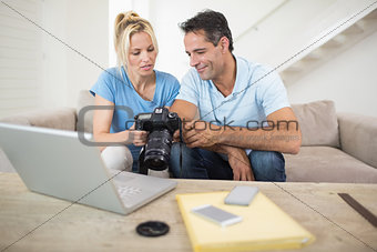 Couple with camera and laptop on sofa in living room