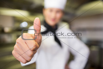 Blurred female cook gesturing thumbs up in kitchen