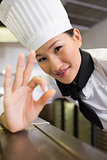 Smiling female cook gesturing okay sign in kitchen