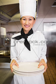 Smiling female cook holding empty plates in kitchen