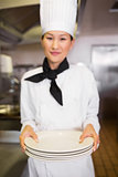 Smiling female cook holding empty plates in kitchen