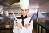 Confident female cook holding knives in kitchen