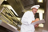 Smiling male cook writing on clipboard in kitchen