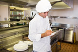 Concentrated male cook writing on clipboard in kitchen