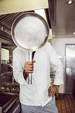 Cook holding pan in front of face in kitchen