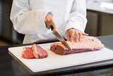 Mid section of hands cutting meat in kitchen