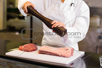 Mid section of female chef grinding pepper over meat