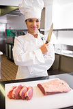 Smiling female chef cutting meat in kitchen