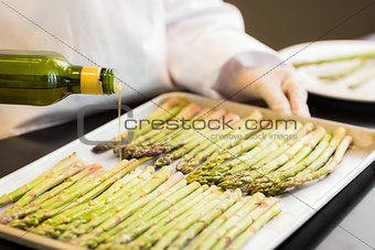 Hand pouring oil on fresh asparagus